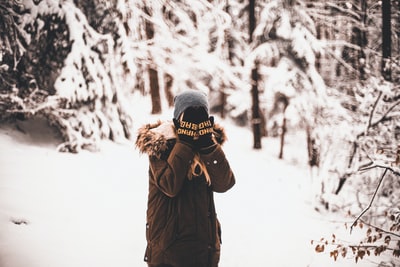 站在被树木包围的雪地上用手捂住脸的人